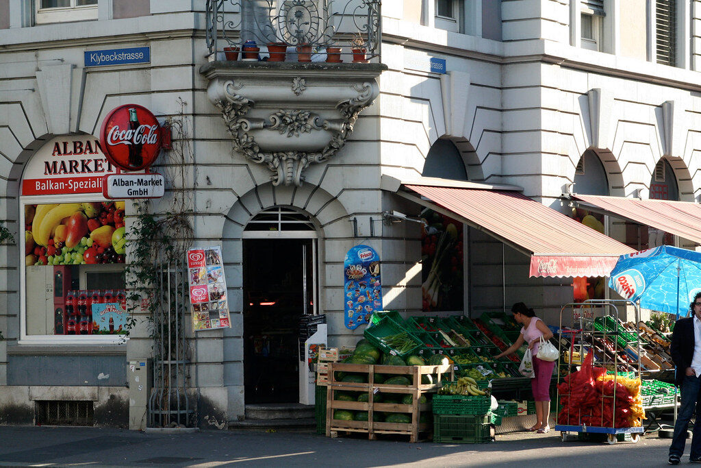 The shopfront of Alban Market, a Balkan grocery at Klybeckstrasse 101 in Basel, with fruit and vegetable crates on the pavement