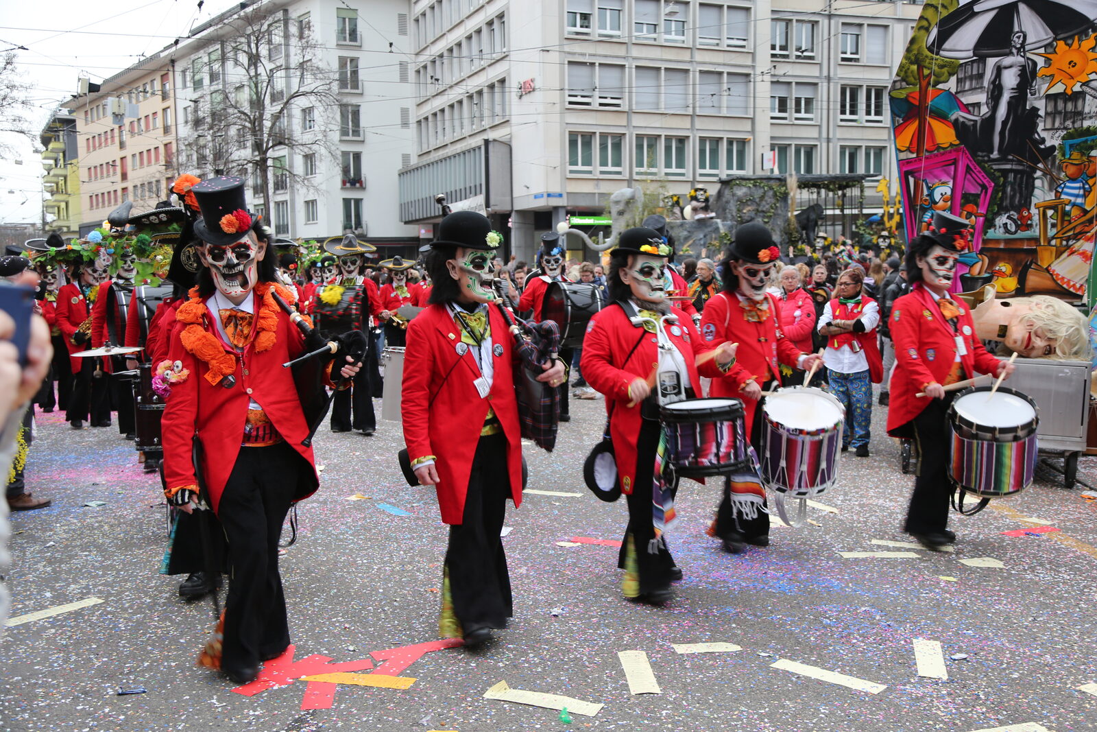 A carnival clique in red uniforms and masks marching with drums and piccolos across Claraplatz in Kleinbasel