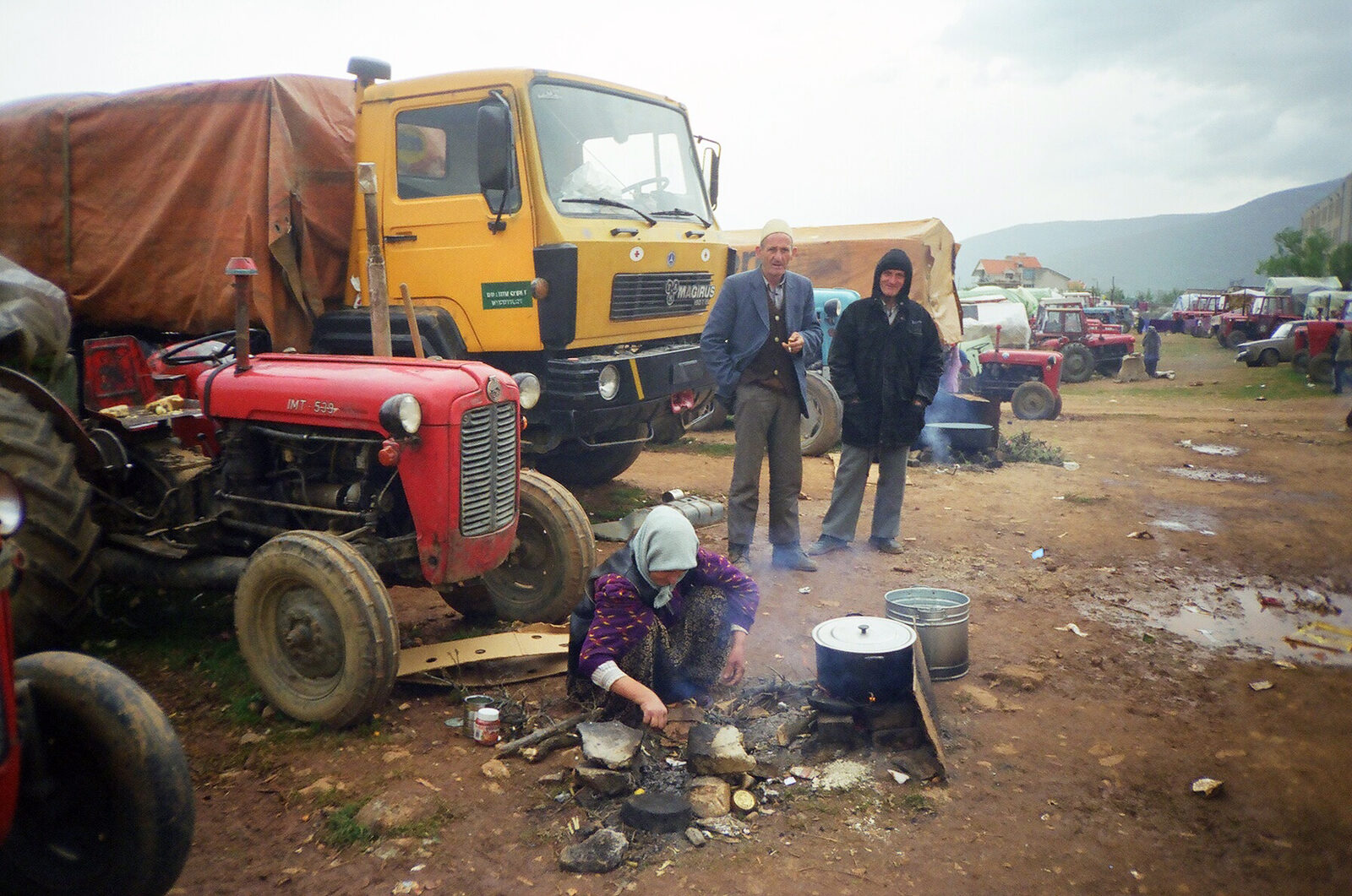 1999'da kuzey Arnavutluk'taki Kukës'te kamp kuran Kosovalı aileler; bir traktör, bir kamyon ve açık ateşte yemek yapan bir kadın