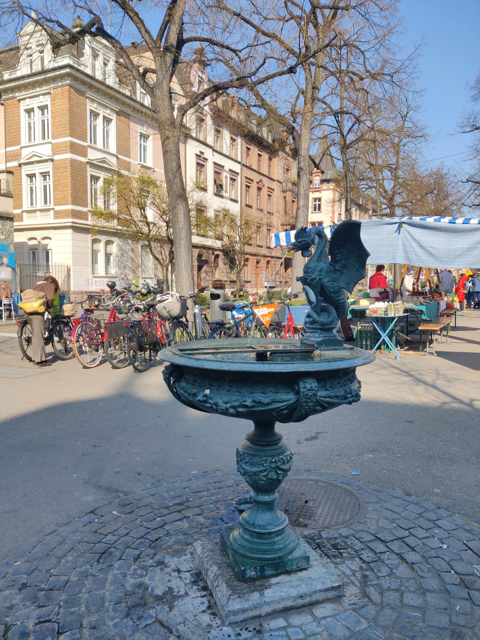 The basilisk fountain on Matthaeusplatz in Kleinbasel with the weekly market behind it
