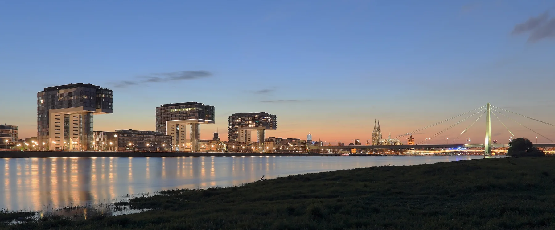 The Kranhäuser, Cologne Cathedral and Severinsbrücke beside the Rhine at dusk.