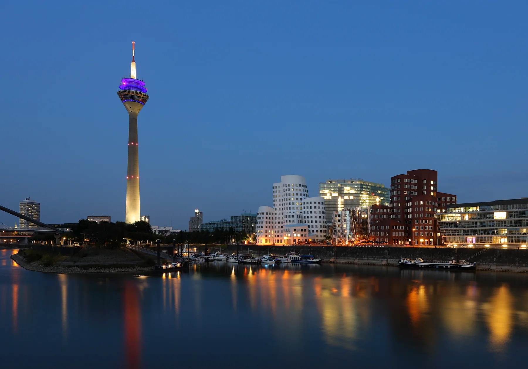 Düsseldorf’s illuminated MedienHafen and Rheinturm reflected in the water at blue hour