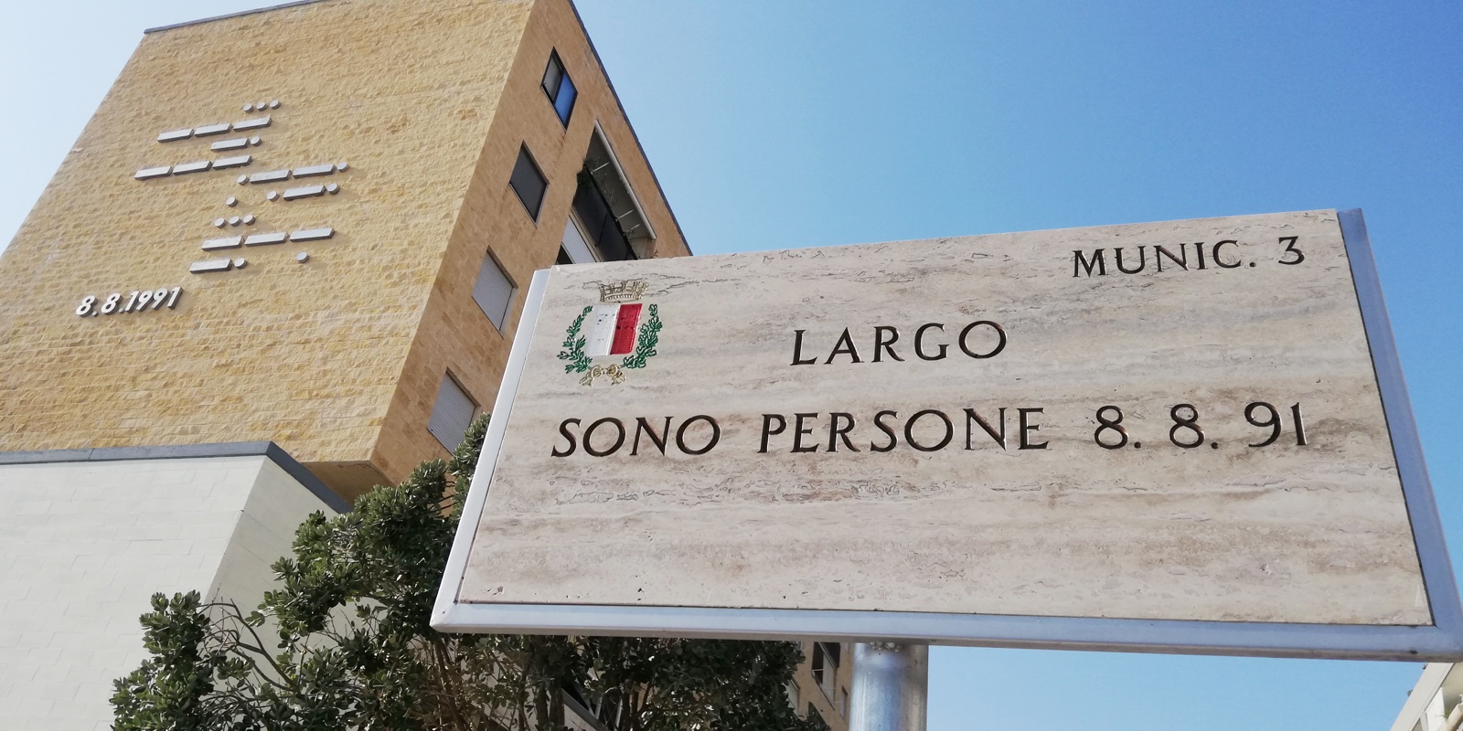 Straßenschild in Bari mit der Aufschrift Largo Sono Persone 8.8.1991, gewidmet der Gastfreundschaft der Baresi und der Landung des Schiffes Vlora