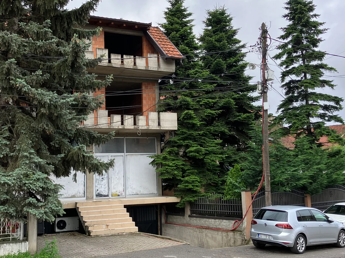 Një shtëpi trekatëshe në një rrugë banimi në Prizren: kati përdhes i përfunduar dhe i xhamuar, ndërsa dy katet sipër janë tulla të zhveshura, me hapje dritareve të zbrazëta nën një kulm gjysmë të mbuluar