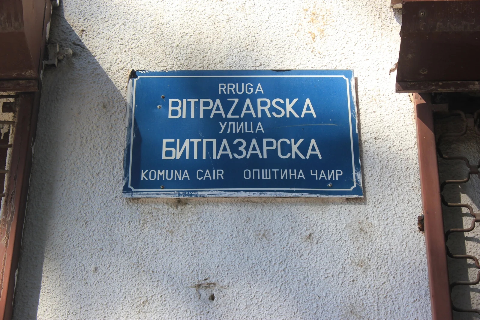 En blå gatuskylt i Skopje med texten Rruga Bitpazarska ovanför Улица Битпазарска