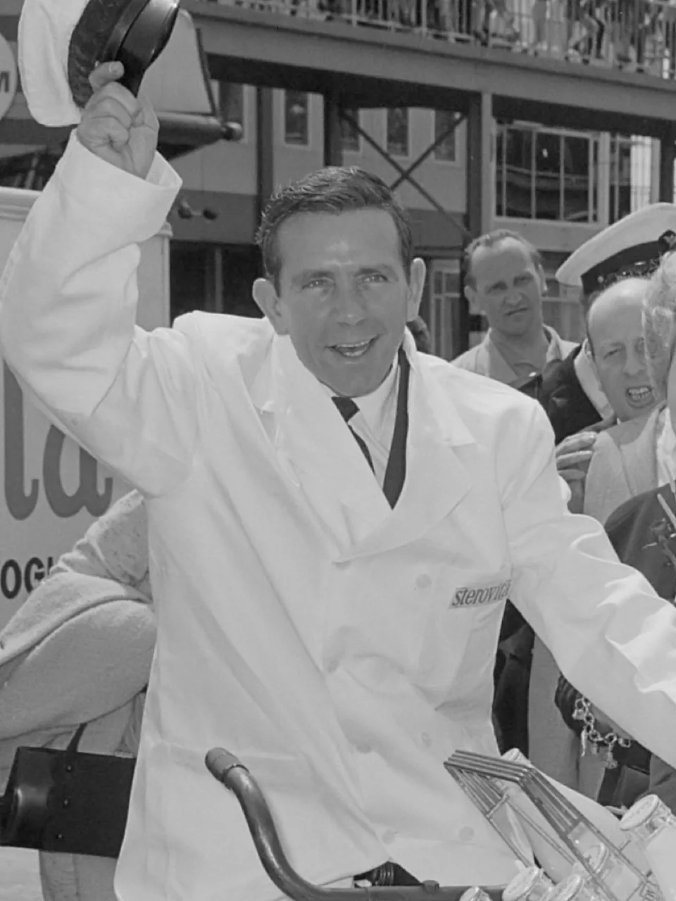 Der Komiker Norman Wisdom in Anzug und Schiebermütze grinst auf einem Pressefoto von 1965 in die Kamera