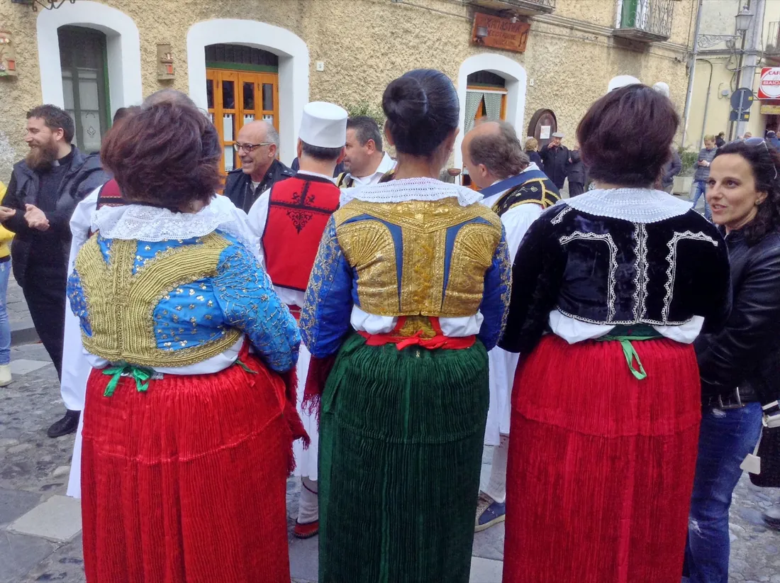 Tres mujeres vistas de espaldas con chaquetas arbëreshë bordadas en oro y faldas plisadas rojas y verdes durante las Vallje en Civita