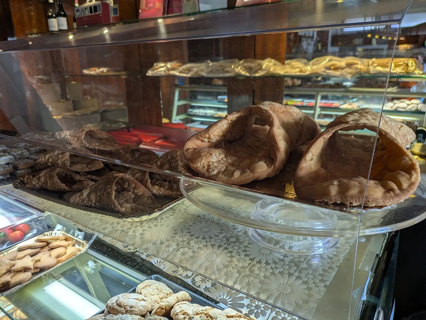 Dos cortezas de cannolo muy grandes sobre un soporte de cristal en una vitrina de pastelería de Extrabar, Piana degli Albanesi