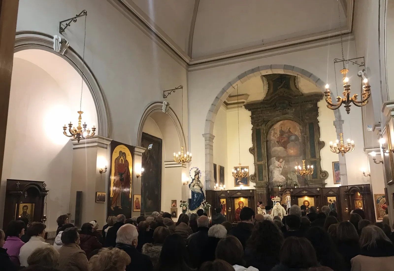 Una iglesia llena en Piana degli Albanesi vista desde el fondo, con el obispo ante el iconostasio y una estatua de la Inmaculada Concepción al lado