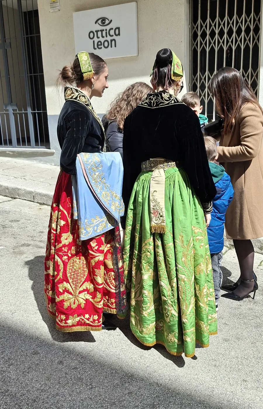 Dos jóvenes con faldas rojas y verdes densamente bordadas con hilo de oro en la procesión del Domingo de Ramos