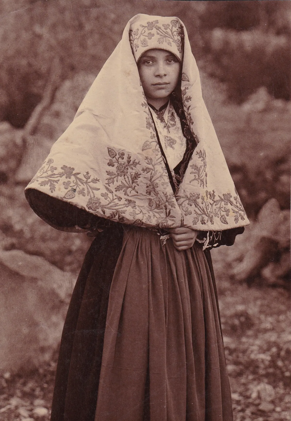 Fotografía en sepia de una joven de Piana degli Albanesi con velo bordado y falda oscura, hacia 1900